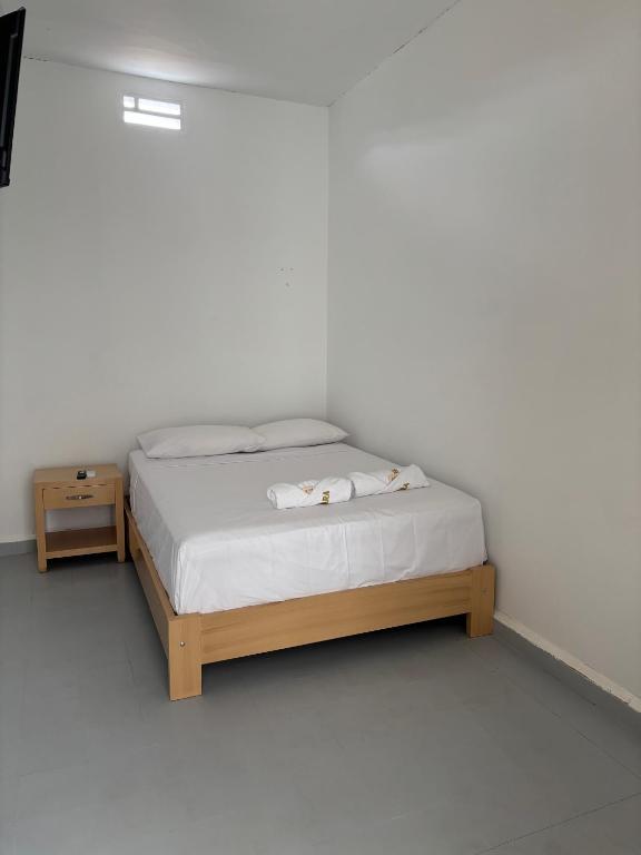 a white bedroom with a bed and a night stand at Hotel Jemara in San Gil