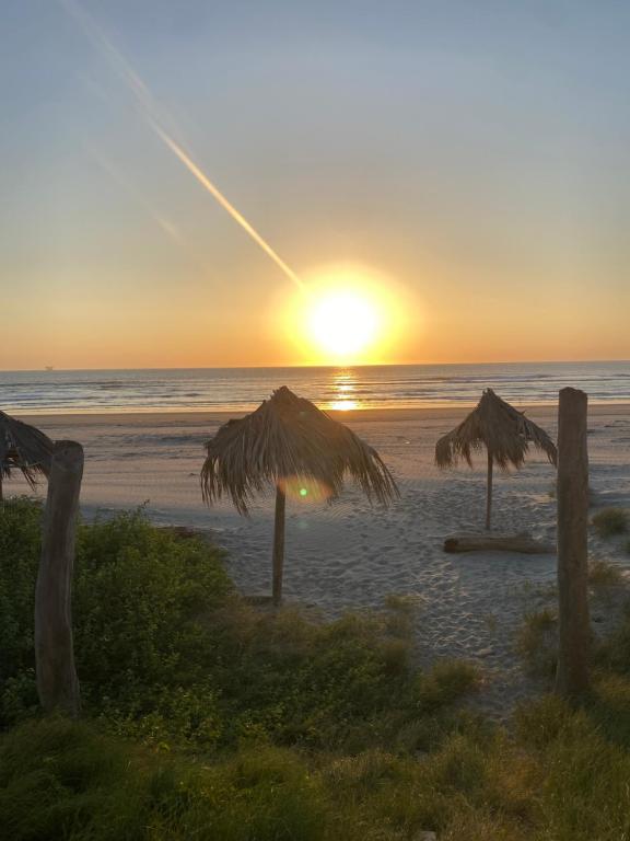 a sunset on the beach with two straw umbrellas at Negritos Beach House in Negritos
