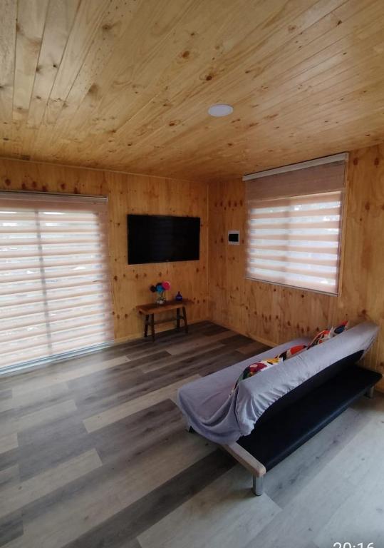 a bedroom with a bed in a wooden room with a tv at Cabaña Rincón de Colbùn in Colbún