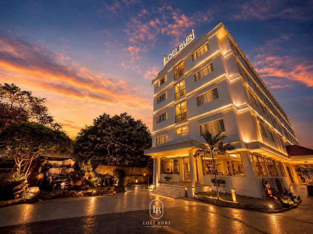 a hotel building with a sunset in the background at Loei Buri Hotel by Alphatel in Ban Tha Phae