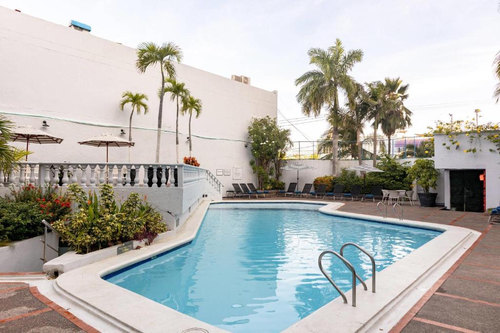 a swimming pool with palm trees and a building at Hotel Faranda Express Puerta Del Sol Barranquilla, A Member of Radisson Individuals in Barranquilla