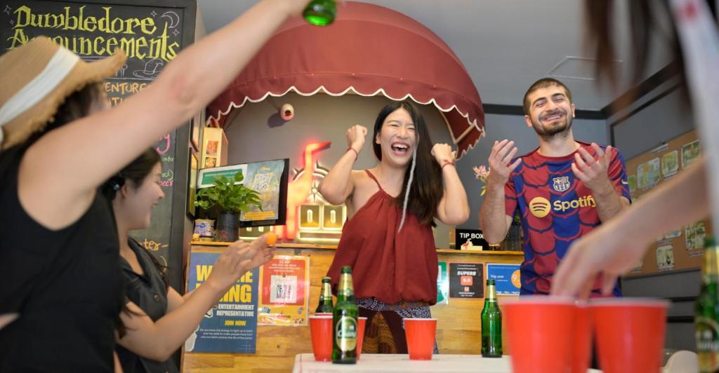 a group of people standing around a table with a woman holding a hot dog at Whoopers Hostel Chiang Mai - Harry Potter Themed in Chiang Mai