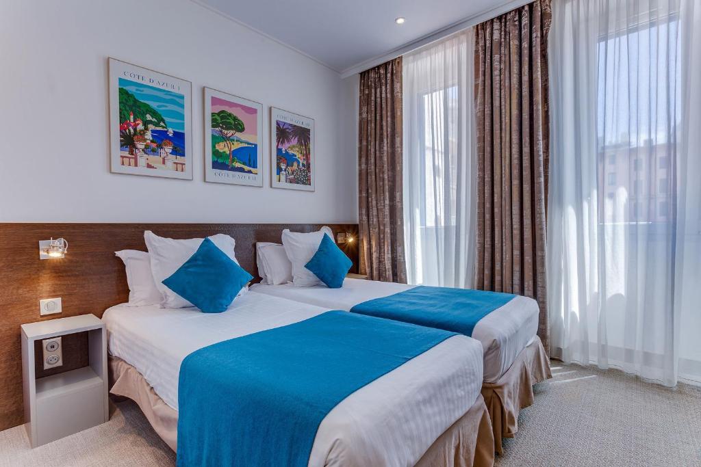 a hotel room with two beds with blue sheets at Hôtel de la Fontaine in Nice