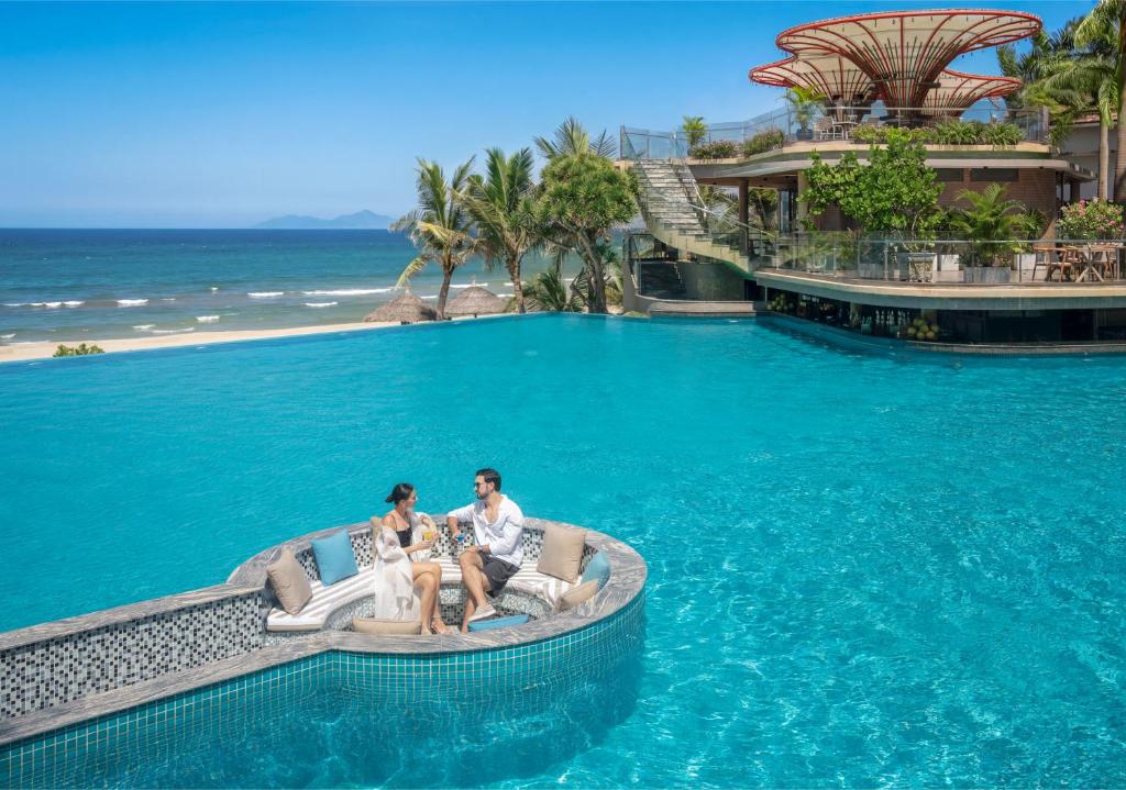 Couple seated on an in-water pool lounge facing the sea.