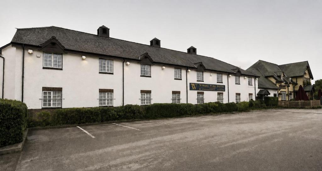 a white building with a parking lot in front of it at Wirral Park Hotel in Greasby