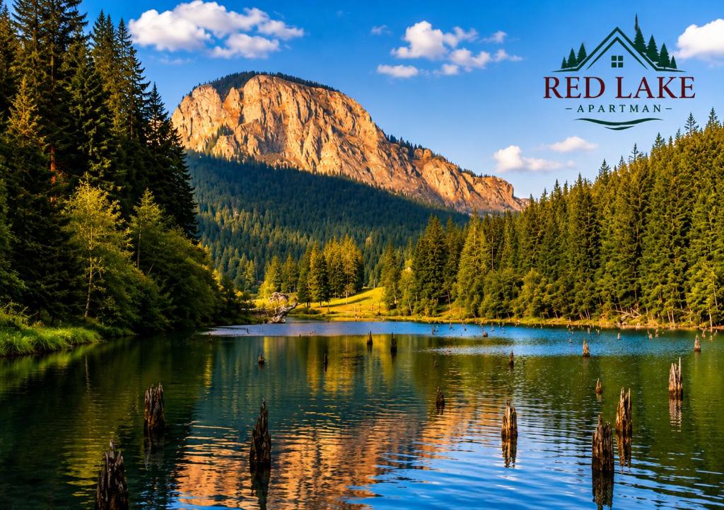 a mountain reflection in a lake with a house at Red Lake Apartman in Lacu Rosu