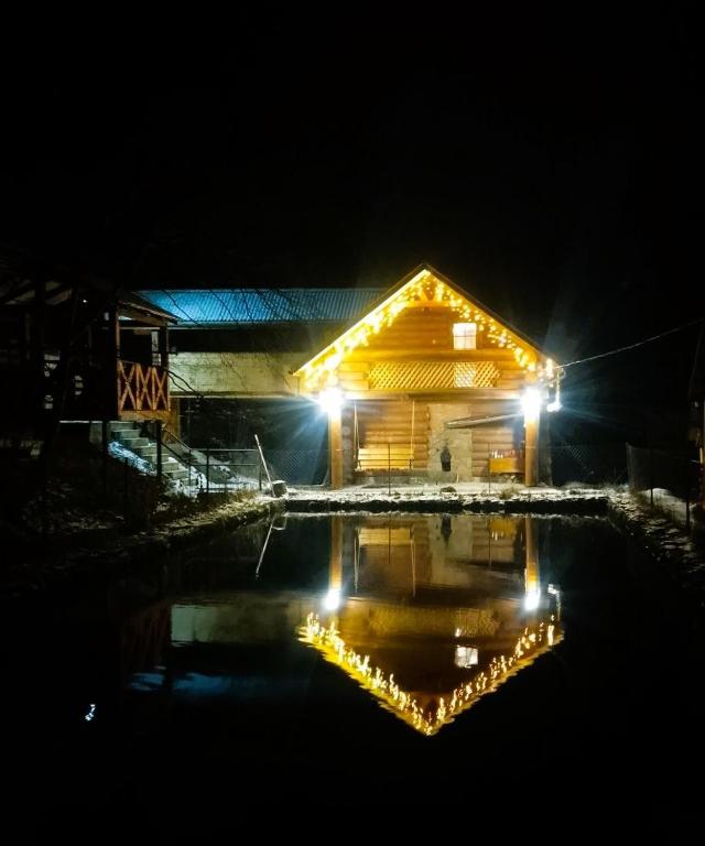 a house lit up at night with lights in the water at Котедж Перша Хата in Synevyrsʼka Polyana