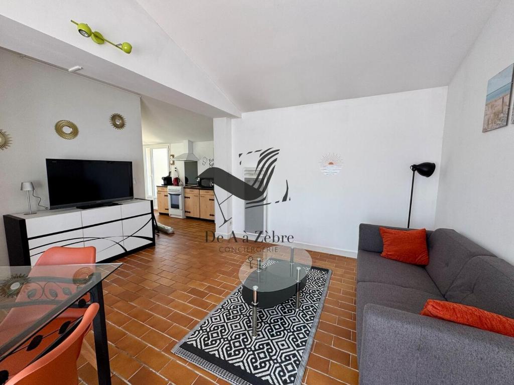 a living room with a couch and a flat screen tv at L'Océane - Maison au calme avec terrasse, centre de Bourg in Le Port-des-Barques