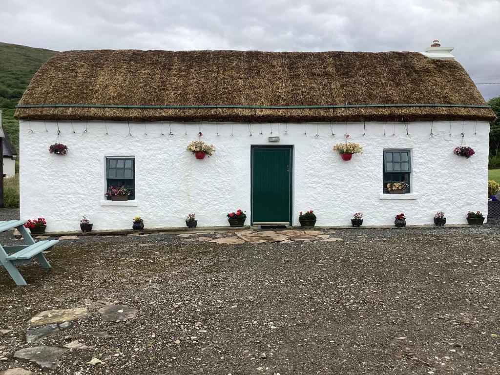 a white building with a thatched roof with a green door at Anne’s Thatched Cottage in Kilcar