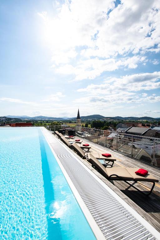 a pool on the roof of a building with lounge chairs at Hotel Randsbergerhof in Cham