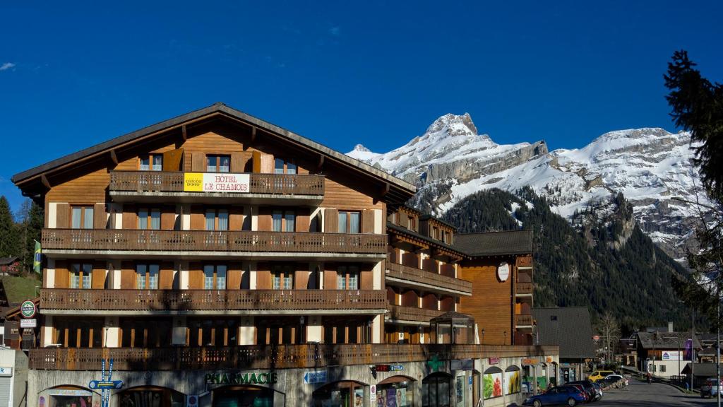 a large wooden building with mountains in the background at Hôtel Le Chamois in Les Diablerets