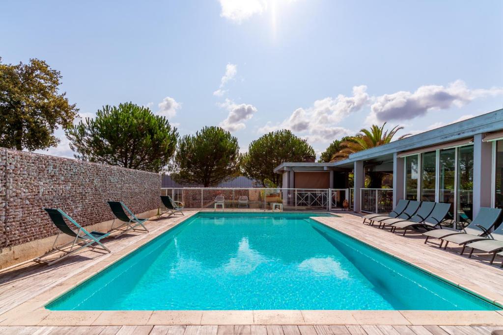 a swimming pool with chairs and a house at Abor Hôtel, Mont de Marsan in Saint-Pierre-du-Mont