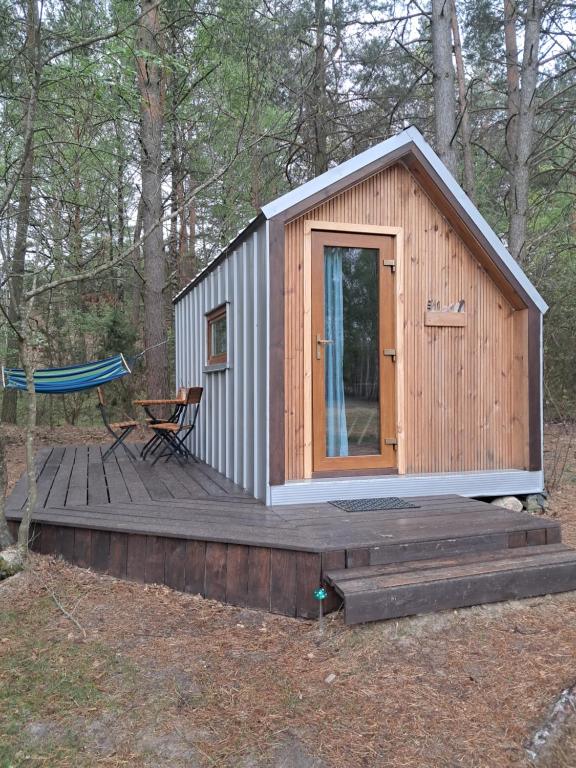 a small cabin with a wooden deck in the woods at Malowane Wrota Camp - Gniazdko in Łazy