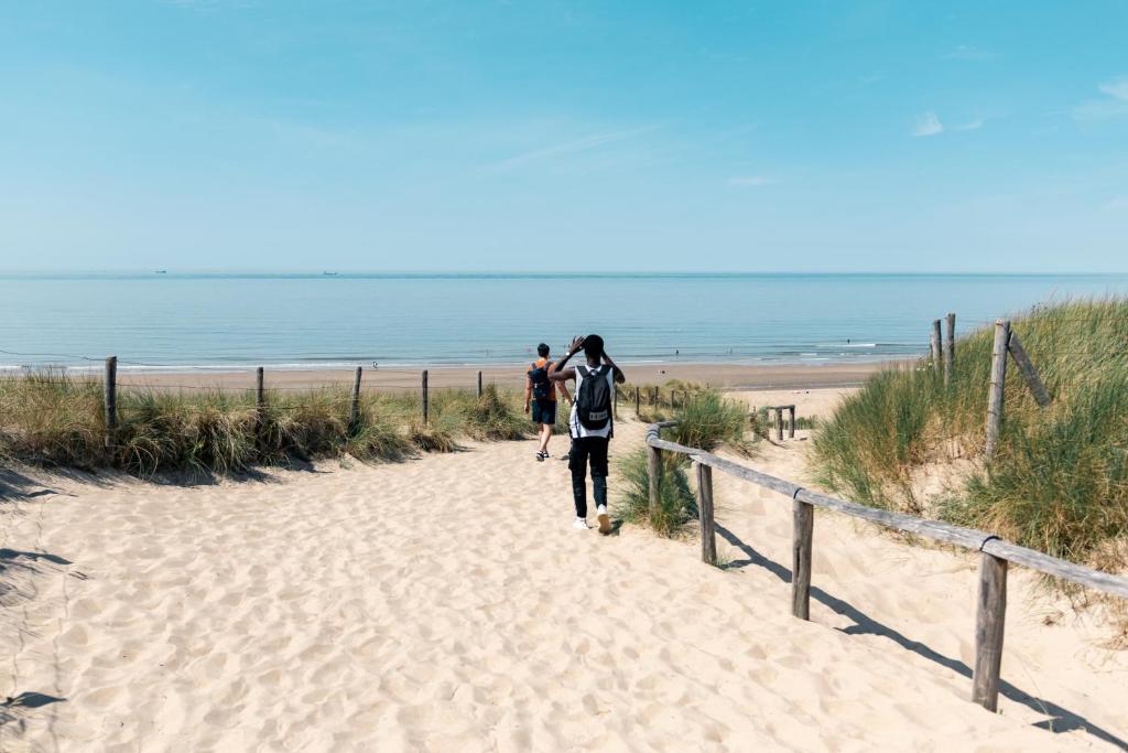 two people walking down a sandy path to the beach at The Flying Pig Beach Hostel Age 18 to 40 in Noordwijk aan Zee