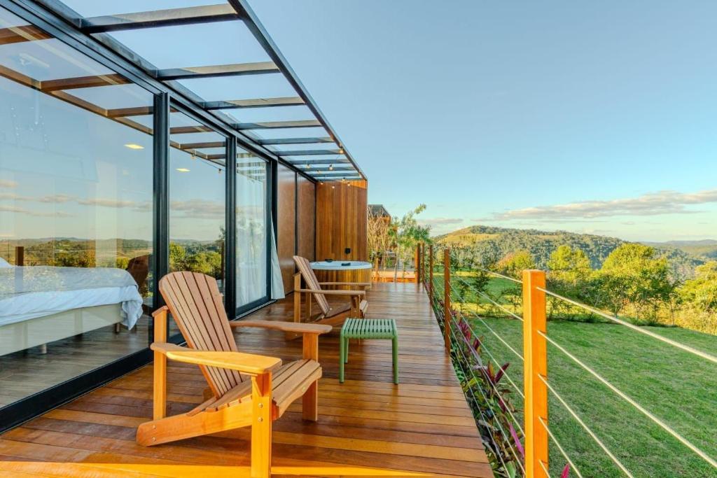 a glass house with a balcony with a bed and chairs at Refúgio Tapera Bungalows & Wellness in Venda Nova do Imigrante