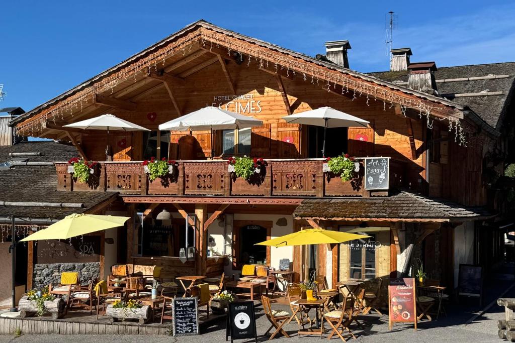 ein Restaurant mit Tischen und Sonnenschirmen vor einem Gebäude in der Unterkunft Chalet-Hôtel & Spa Les Cimes in Le Grand-Bornand