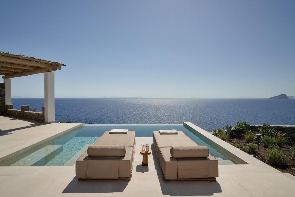 a swimming pool with two lounge chairs and the ocean at AOTO Villas in Kithnos