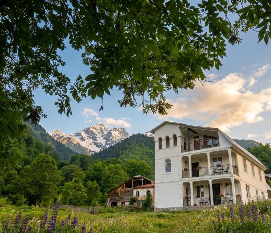 a white house with mountains in the background at Nakra Tower GuestHouse in Mestia