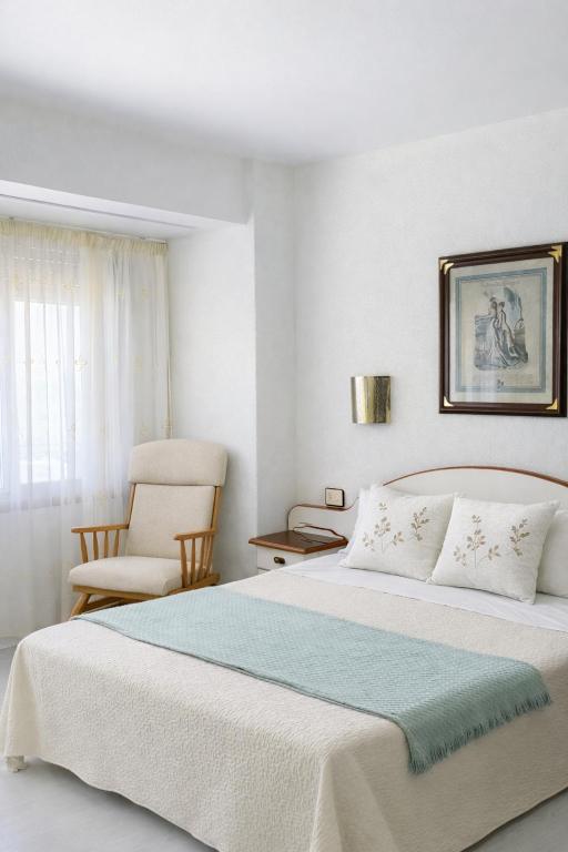 ein weißes Schlafzimmer mit einem Bett und einem Stuhl in der Unterkunft Hostal J.B in Malpica