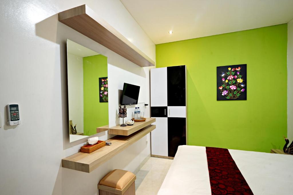a bedroom with green walls and a bed and a television at D'Pande Kuta in Kuta