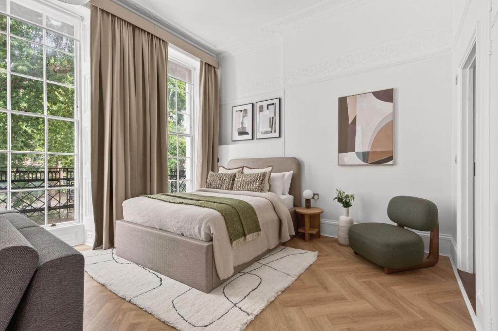 a bedroom with a bed and a chair and windows at GuestReady - The Crescent in London