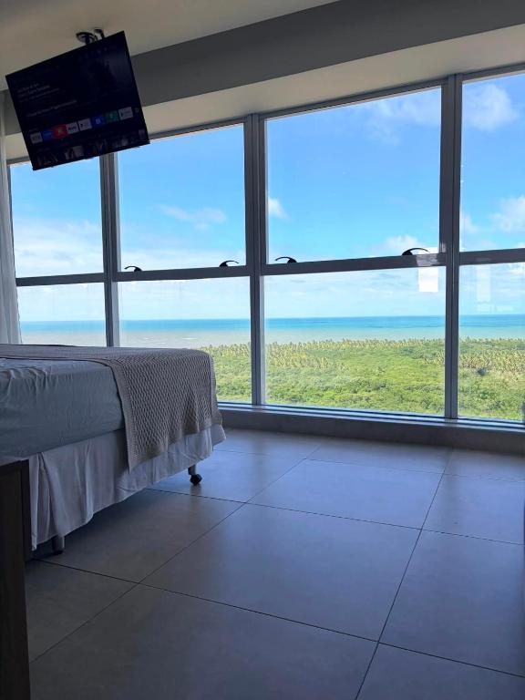 a bedroom with large windows and a flat screen tv at Bugan Premium 16 andar - vista mar incrível in Recife