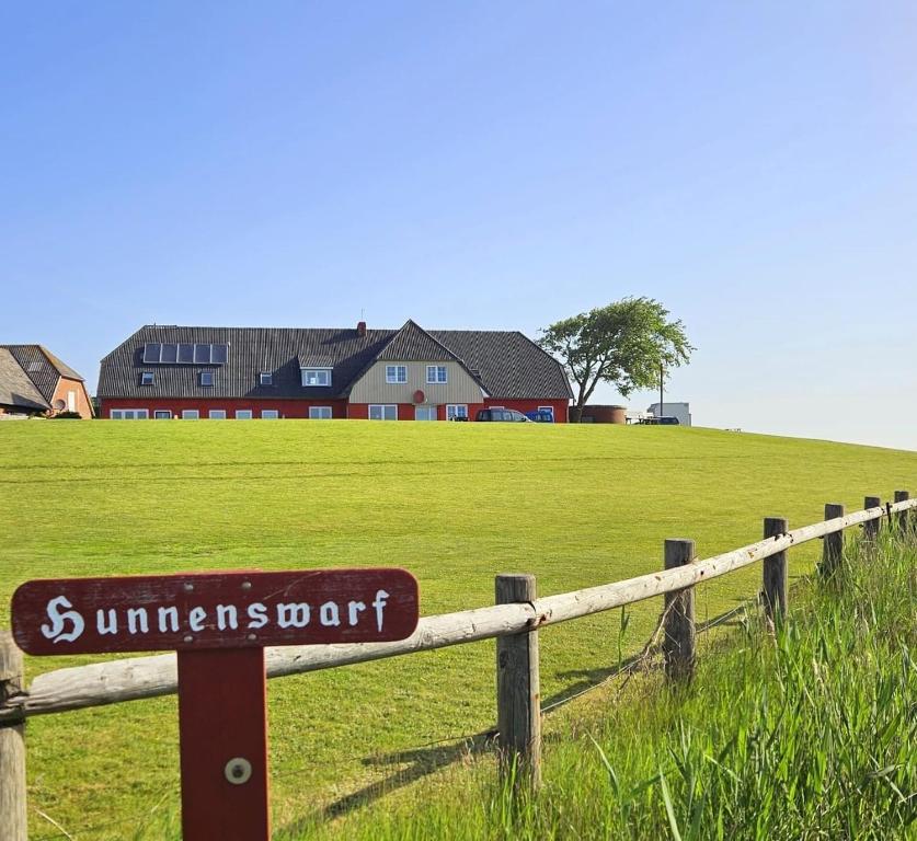 a sign on a fence in a field with a house at HaRE Ferienwohnungen Käptn Magda in Langeneß