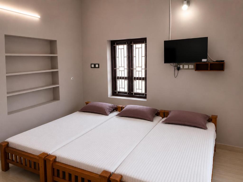 two beds in a room with a tv on the wall at Hotel Sabareesh Kanyakumari in Golden Rock