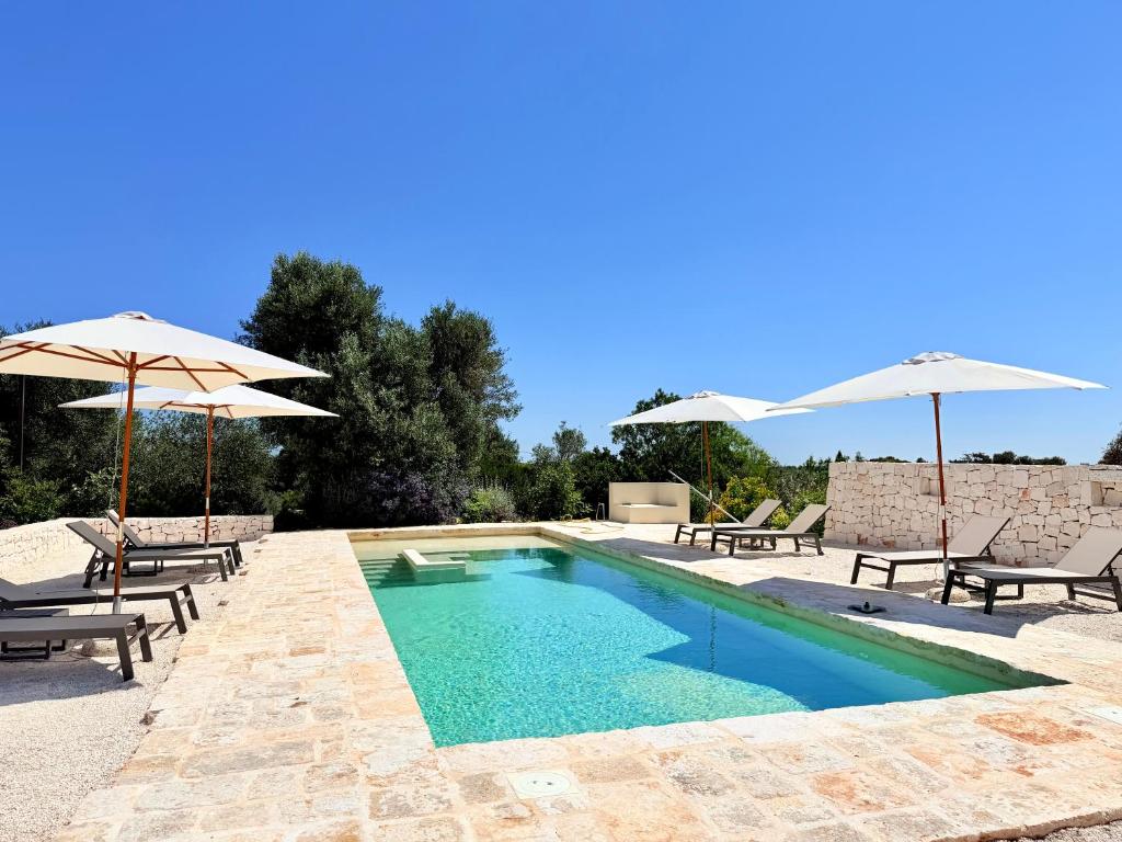 a swimming pool with two umbrellas and chairs and a pool at Trullo botanico in Ceglie Messapica