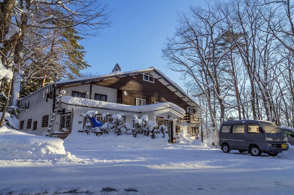 a house covered in snow with a van parked in front at Pension Starlight Azumi in Hakuba