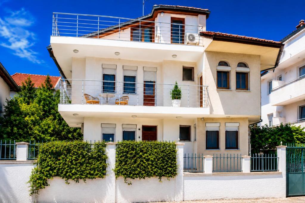 a white house with a fence and bushes at Summerbreath Apartments in Ahtopol