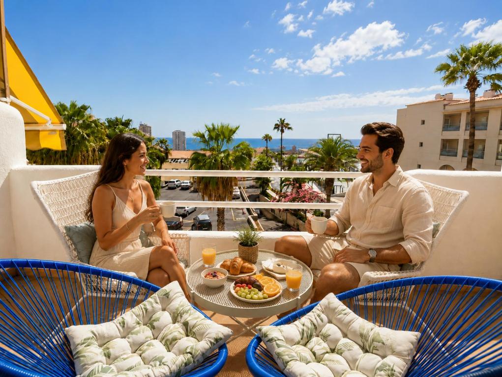 a man and a woman sitting on a balcony with food at Modern 1BR Ocean View with AC and Pool in Costa Adeje by Aqua Vista Tenerife in Adeje
