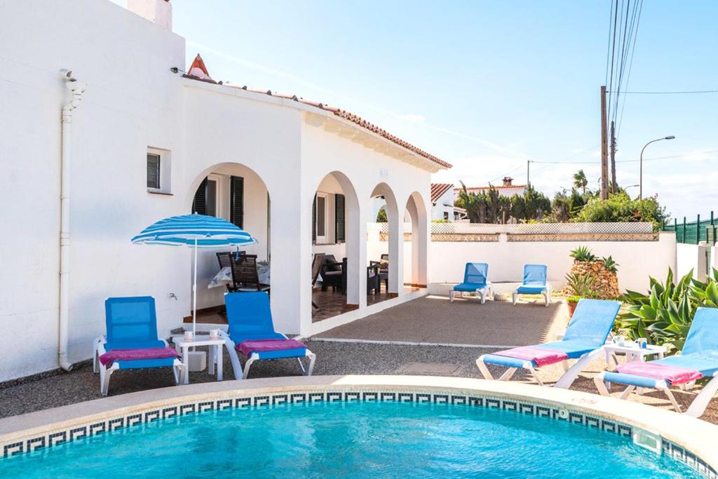 a swimming pool with chairs and an umbrella next to a house at Villa Dulcesol by Villa Select in Alaior