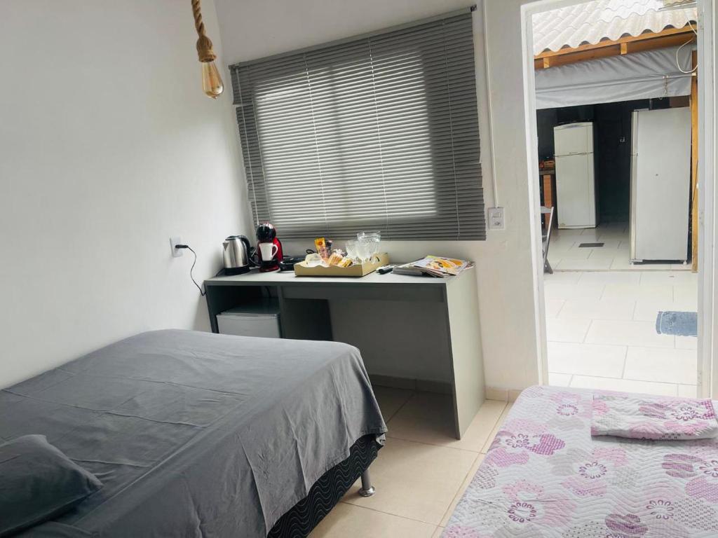 a bedroom with a bed and a desk and a kitchen at Pousada Coral in Osório