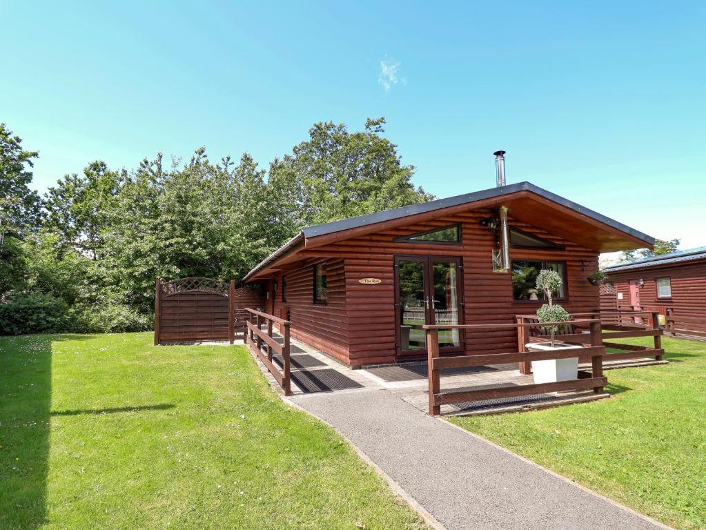 a wooden cabin with a porch and a grass yard at The Roe in St Asaph
