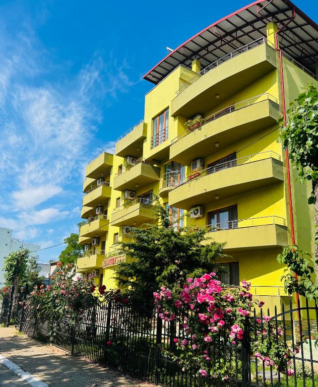 a yellow building with flowers in front of a fence at Hotel Angely in Eforie Nord