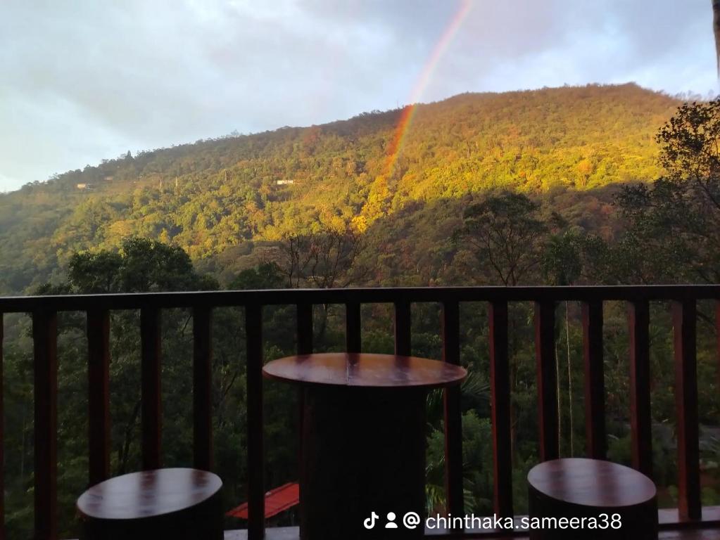 a rainbow over a mountain with a table on a balcony at Wishparing fall villa laxapane in Kiriwan Eliya