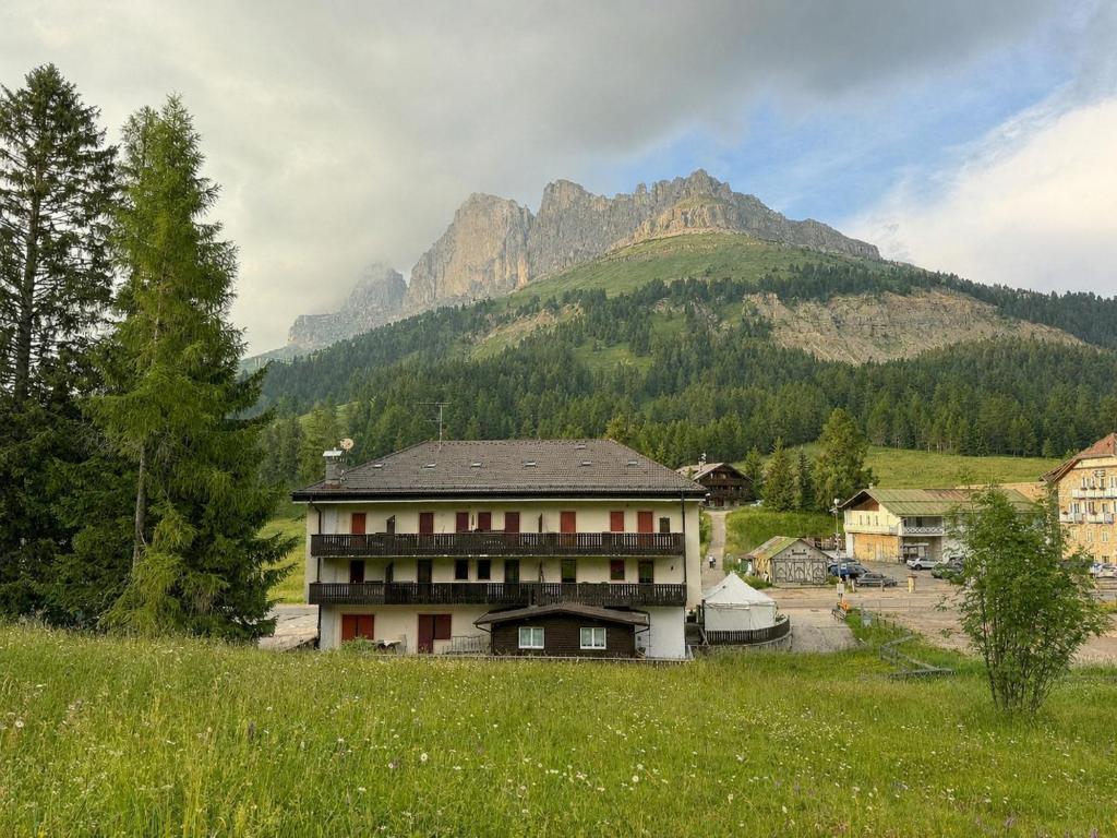 a building in a field with a mountain in the background at Passo Carezza Club Apartment in Carezza al Lago