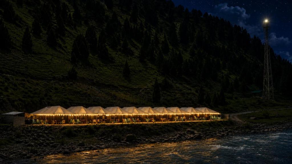 a lit up tent next to a river at night at GUREZ LUXURY Resort by GRITTI CASTLE in Wāmpor