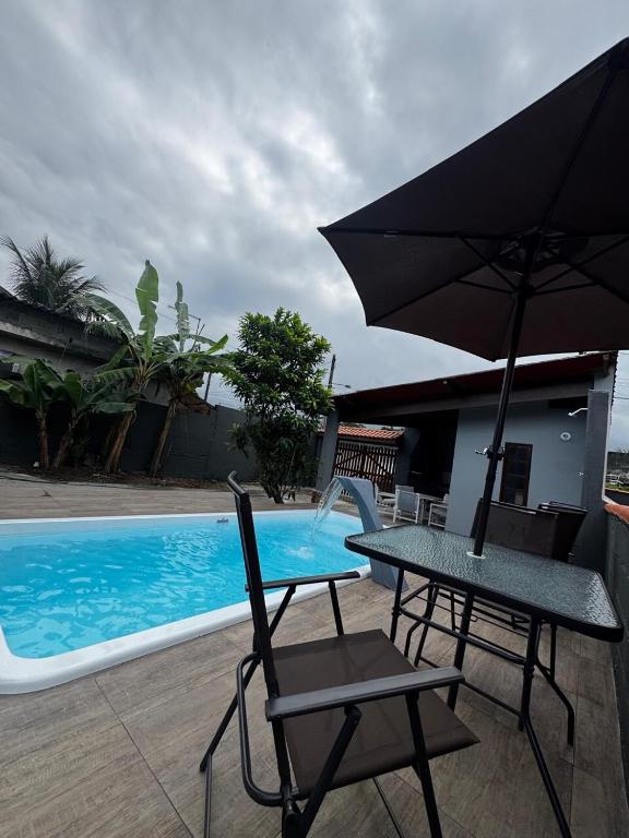 a table and chairs with an umbrella next to a swimming pool at Casa de Praia com Piscina e Espaço Gourmet in Bertioga