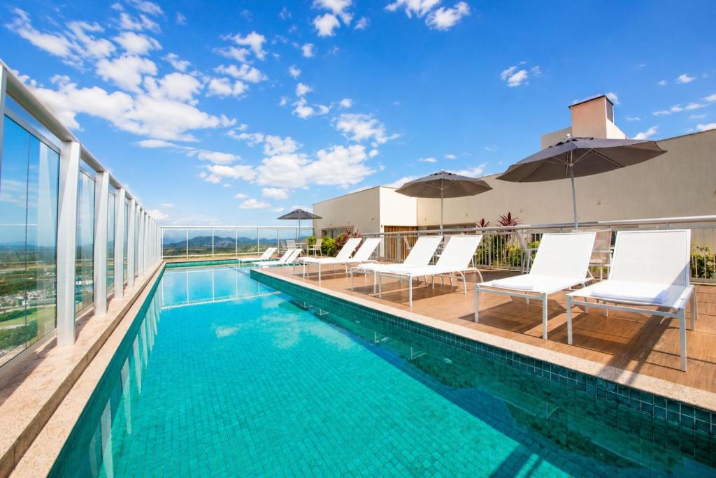 a swimming pool with white lounge chairs and an infinity at Promenade Fusion Itaguaí in Itaguaí