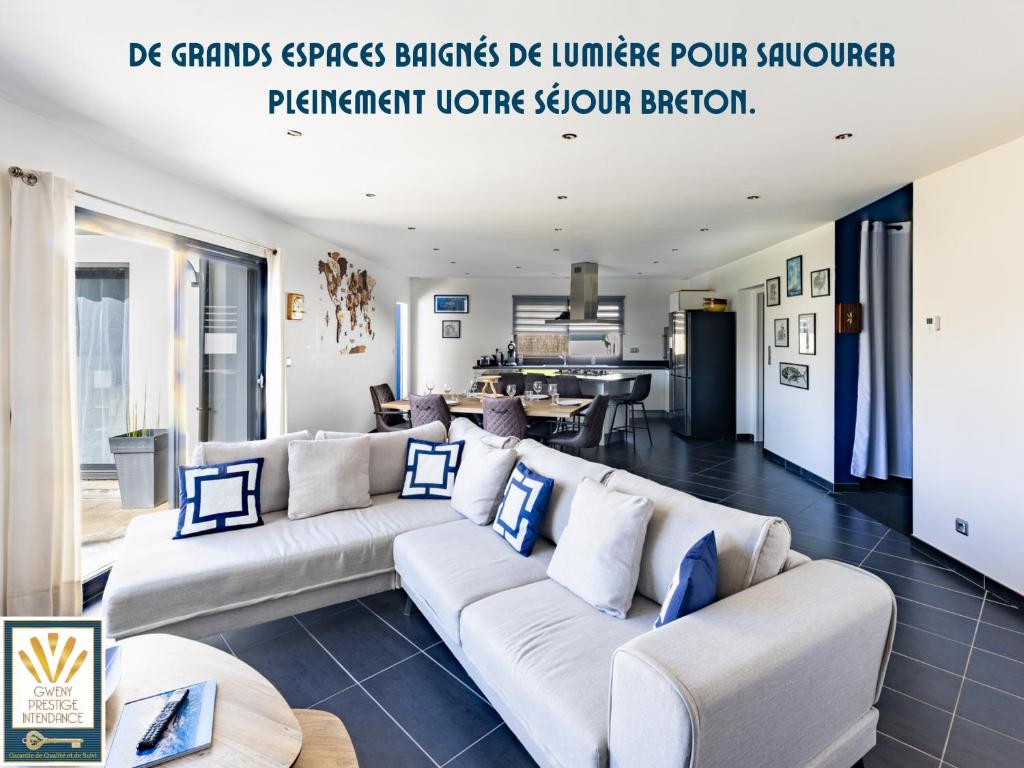 a living room with white couches and a kitchen at Les Alizés in Plouhinec