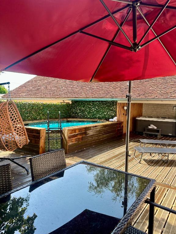 a red umbrella on a deck with a swimming pool at La Longère du Menuisier : Spa-Châteaux-Beauval in Romorantin