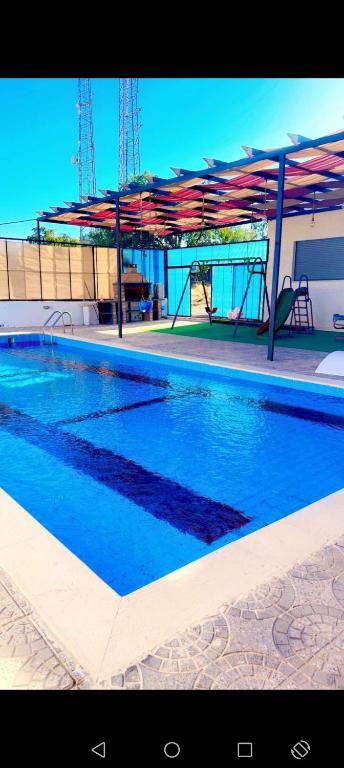 a swimming pool with blue water and red umbrellas at Albaraka-farm in Az Zarqa