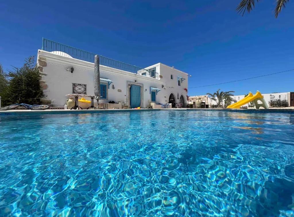 a swimming pool with blue water in front of a house at La maison des oliviers in Houmt Souk