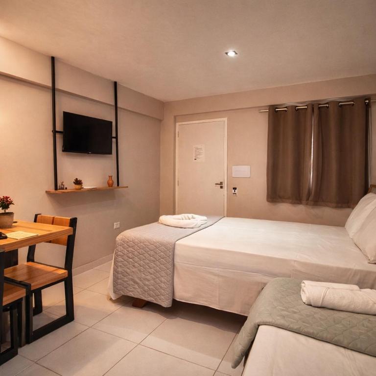 a bedroom with two beds and a table and a television at Pousada BOB Suítes in Porto De Galinhas