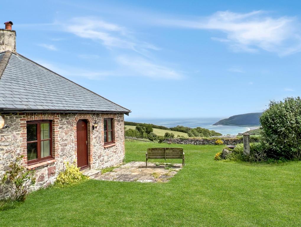 a stone building with a bench next to the ocean at Beehive Cottage Culbone in Porlock