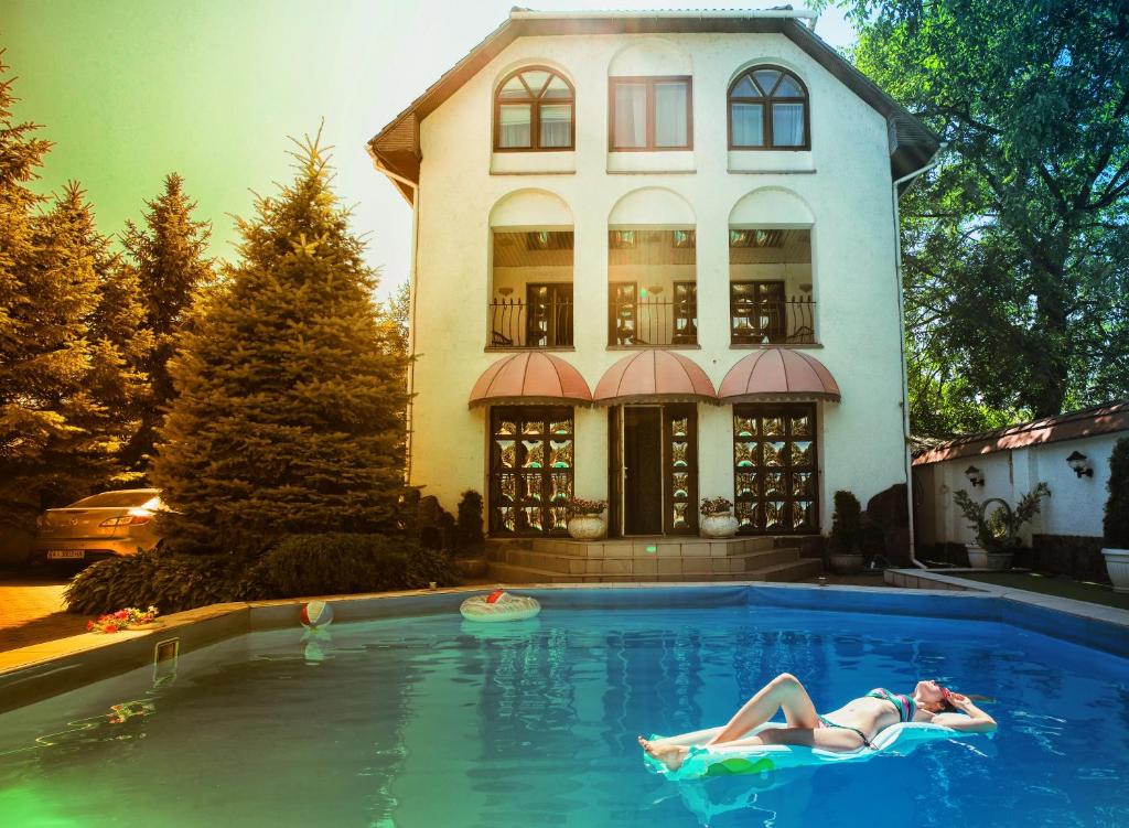 a woman laying in a swimming pool in front of a house at Eduard Hotel in Uzhhorod