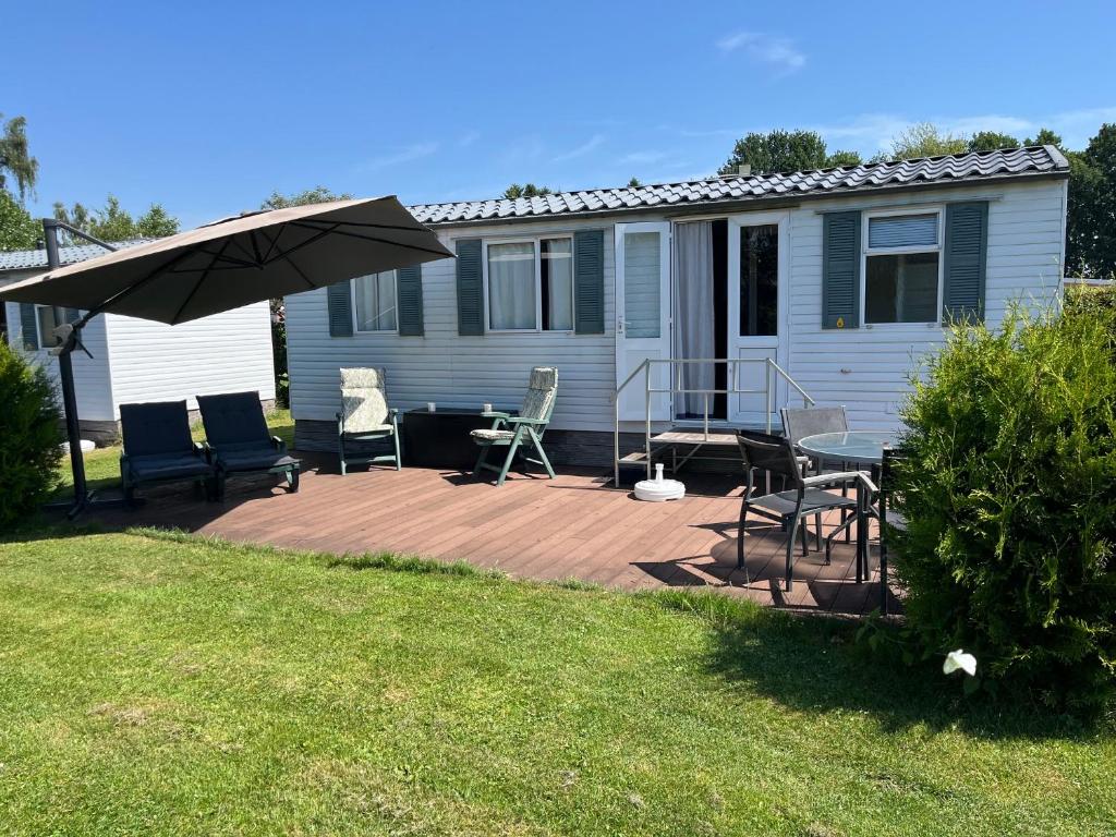 a deck with chairs and an umbrella in front of a house at Camping BuitenRijk - Chalet D35 Huisdier vrij in Valthermond
