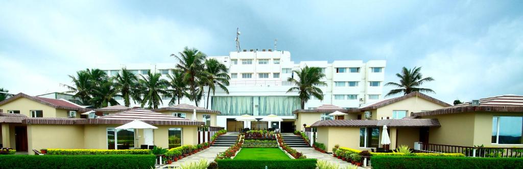 a large white building with palm trees in front of it at Hotel Holiday Resort in Puri